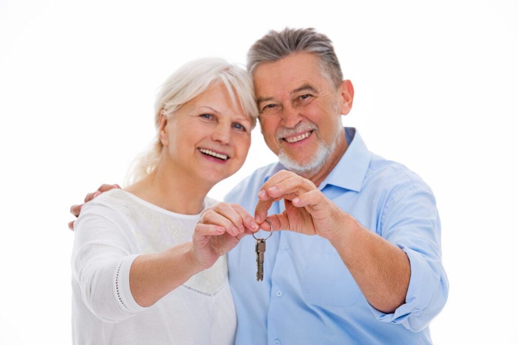 Älteres Paar hält gemeinsam einen Hausschlüssel vor weißem Hintergrund