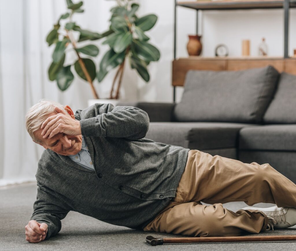Älterer Mann liegt auf dem Boden im Wohnzimmer neben einem Gehstock