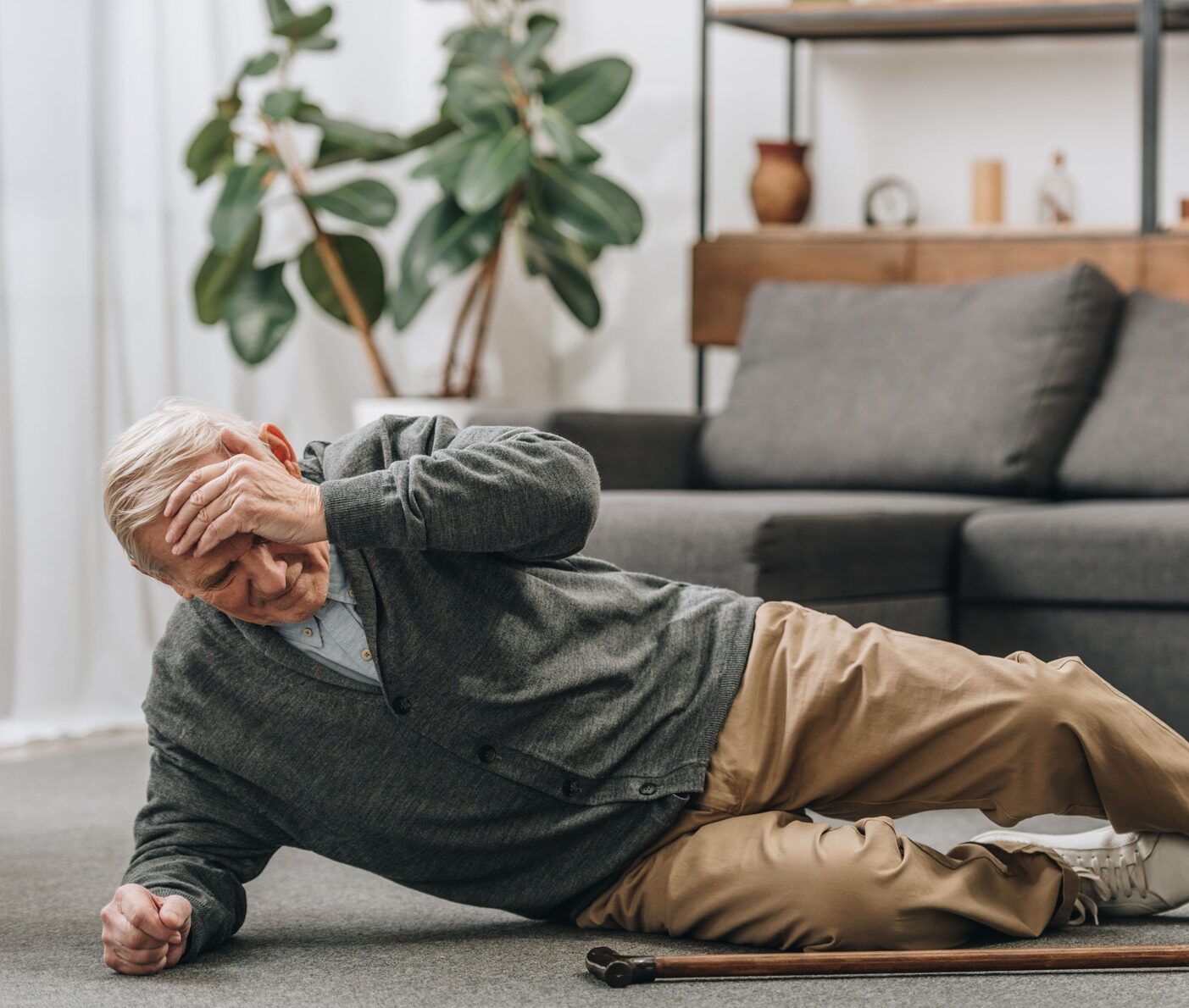 Älterer Mann liegt auf dem Boden im Wohnzimmer neben einem Gehstock