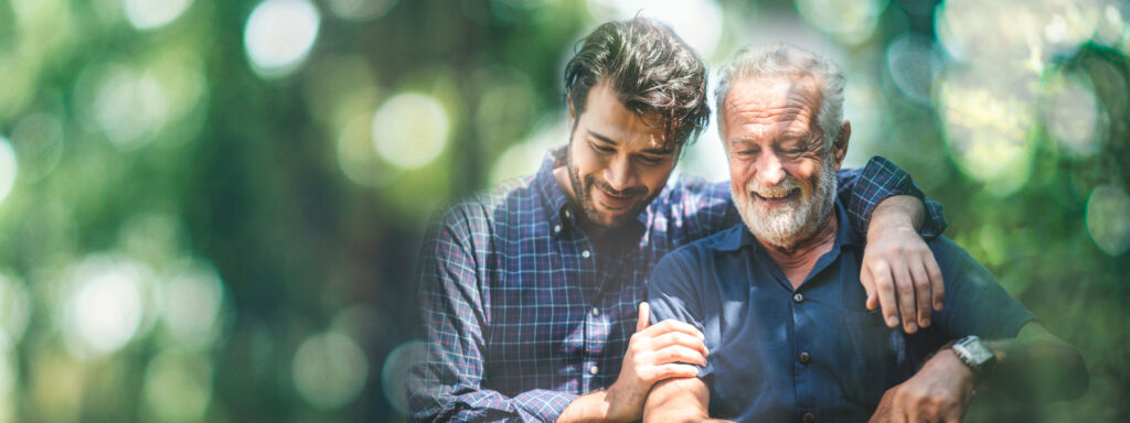 Jüngerer Mann umarmt älteren Mann im Freien, beide tragen Hemden, freundliche Geste