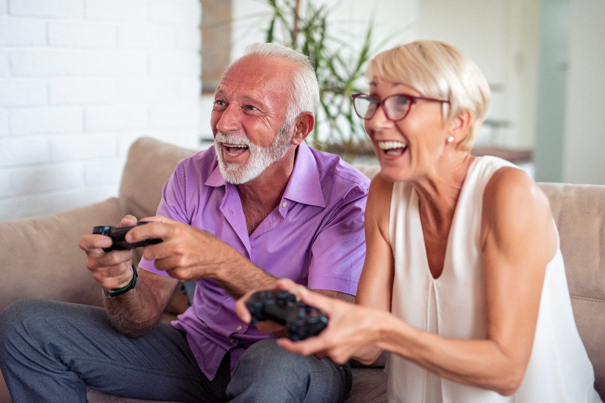 Älteres Paar sitzt auf Sofa und spielt Videospiele mit Controllern in den Händen