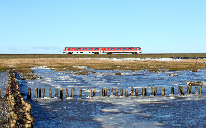 Zwei rote Regionalzüge fahren auf einer Bahnstrecke durch eine offene Winterlandschaft