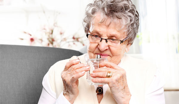 Eine Seniorin riecht an einer Parfüm-Flasche. 