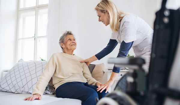 Eine ältere Dame wird von einer 24 Stunden Kraft am Bett unterstützt, um in den Rollstuhl zu kommen.