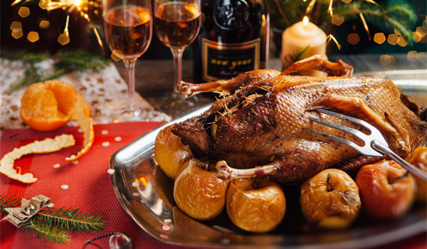 Eine fertige Weihnachtsgans auf einem dekorierten Tisch. Dazu gibt es zwei Gläser Sekt.