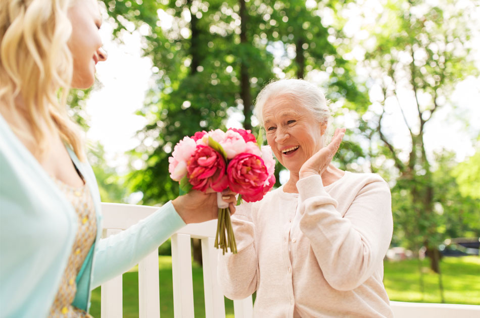Eine junge Frau überreicht einer älteren Dame einen Blumenstrauß.
