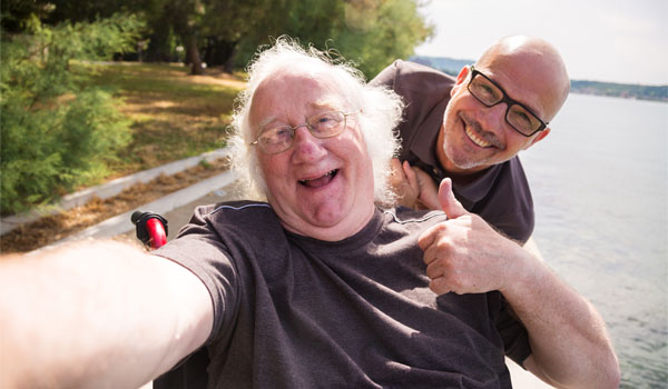 Ein behinderter Mensch ist im Rollstuhl mit seinem pflegenden Angehörigen unterwegs.