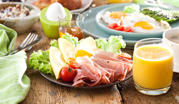 Frühstückstisch mit Ei, O-Saft und einem Teller mit Wurst und Käse.