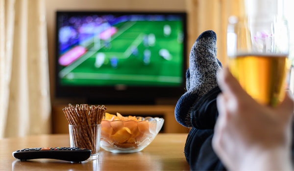 Fußball zuhause allein im TV schauen mit Chips und Salzstangen auf dem Tisch.