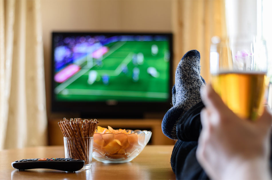 Fußball zuhause allein im TV schauen mit Chips und Salzstangen auf dem Tisch.