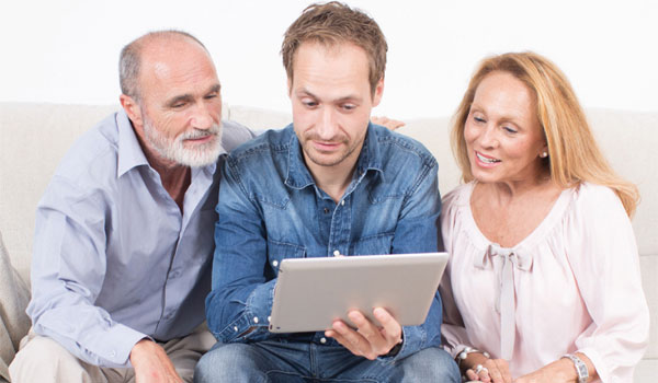 Sohn sitzt mit Eltern auf der Couch. In seiner hand ein Tablett mit dem er die Kosten für einen Hausnotruf berechnet.