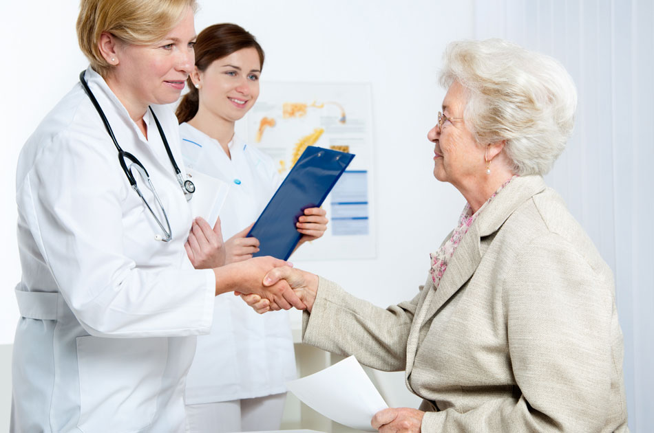 Krankenhausnachsorge: Eine Ärztin schüttelt einer Patientin, die das Krankenhaus verlässt, die Hand. Neben ihr steht eine Krankenschwester.