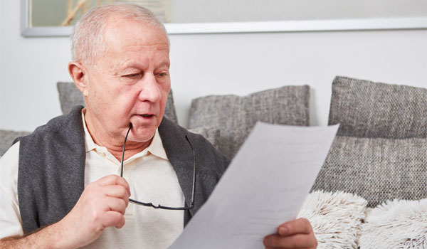 Ein Senior liest auf seiner Couch ein Schreiben von seiner Krankenkasse.