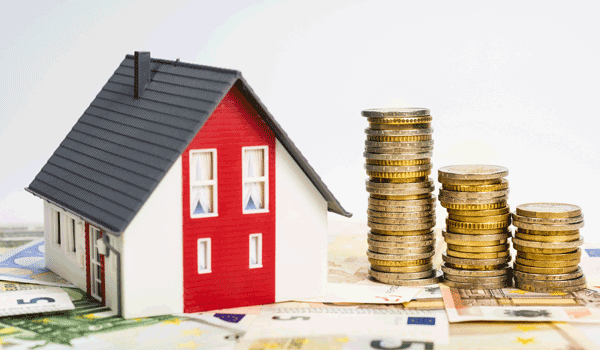 Ein Modellhaus auf Geldscheinen. Daneben ein drei gestapelte Geldberge.