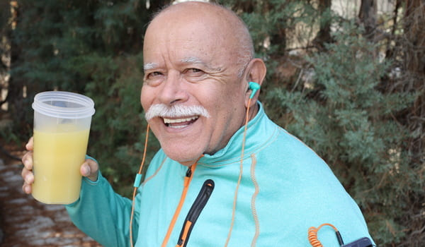 Ein Senior in sportlicher Kleidung trinkt einen Mahlzeitenersatz in Shake-Form.