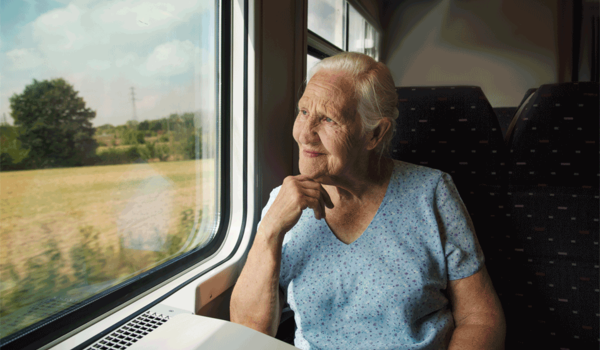 Eine Seniorin reist mit dem Zug und schaut aus dem Fenster.