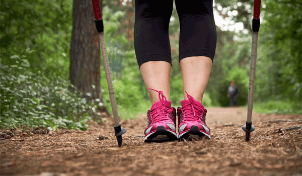 Eine Frau beim Nordic Walking. Zu sehen sind nur die Stöcke und ihre Beine.