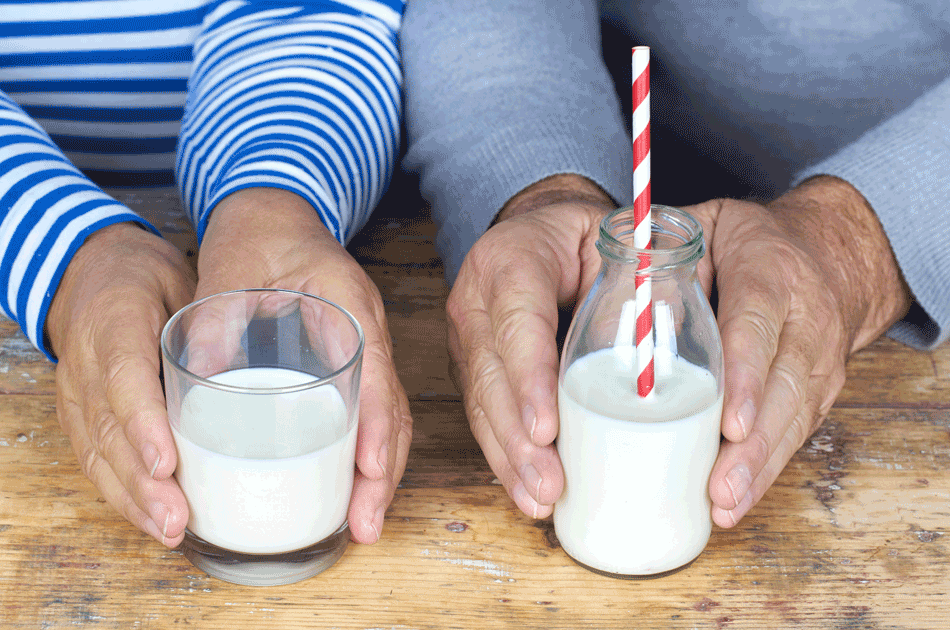 Zwei Senioren halten jeweils ein Glas Milch in die Kamera.
