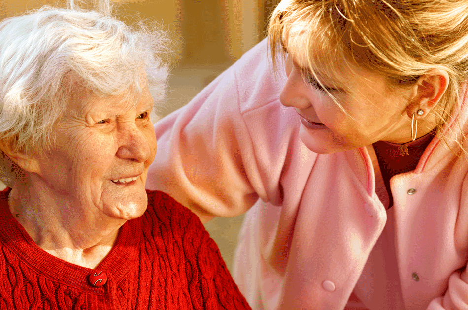 Die Tochter beugt sich zu Ihrer Demenzkranken Mutter, die auf dem Stuhl sitzt.