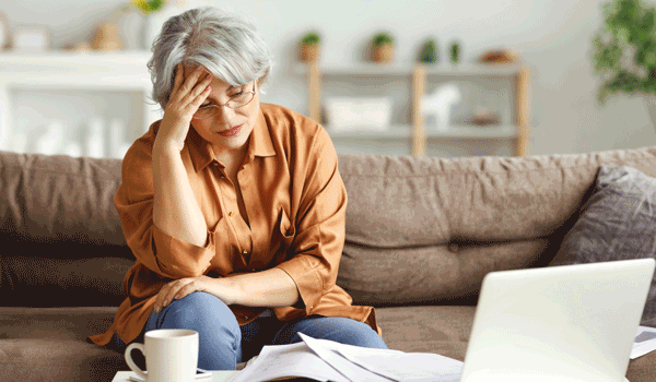 Eine pflegende Angehörige sitzt gestresst auf ihrem Sofa. 