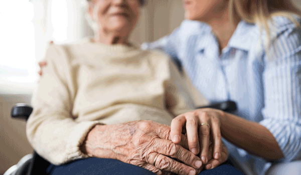 Eine Tochter kniet neben ihrer Mutter, die im Rollstuhl sitzt. 