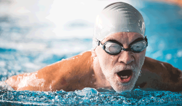 Ein älterer Schwimmer beim Brustschwimmen. Er taucht gerade auf um Luft zu holen.