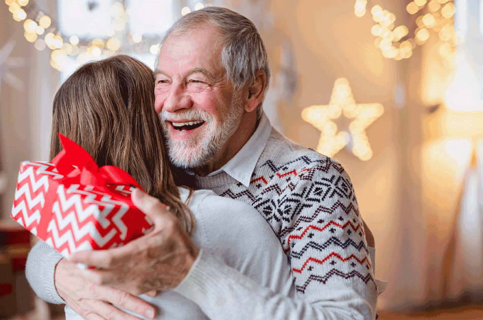 Ein Senior bekommt ein Geschenk zu Weihnachten und umarmt aus Dank seine Tochter.