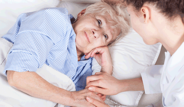 Eine Pflegerin kümmert sich um eine Seniorin, welche im Bett liegt und zufrieden schaut.