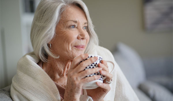 seniorin, eingehüllt in einer decke, trinkt im wohnzimmer tee