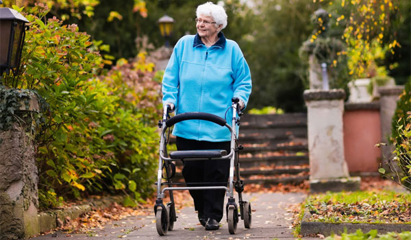 eine Seniorin mit Rollator unterwegs, in einem herbstlichen Park.