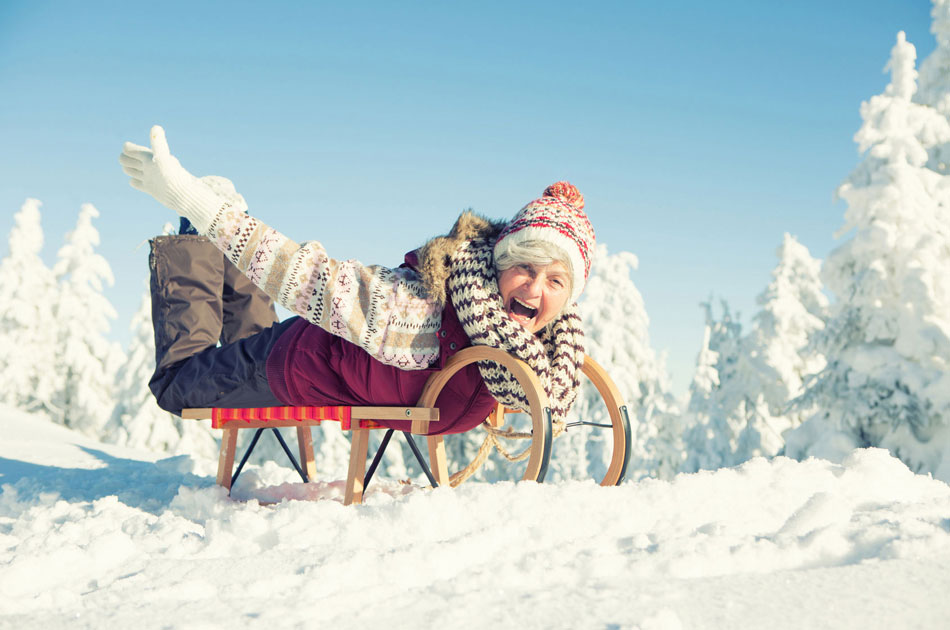 Seniorin fährt mit einem Schlitten, auf dem Bauch liegend, durch den Schnee.