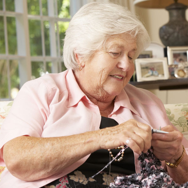 Rentnerin strickt sitzend im Sessel.