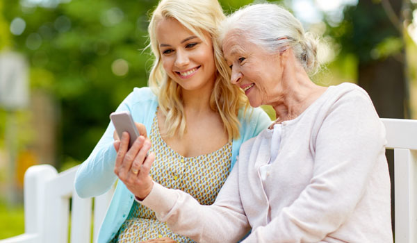 Tochter erklärt ihrer Mutter die Nutzung des Handys. Beide sitzen auf einer Bank im Park.