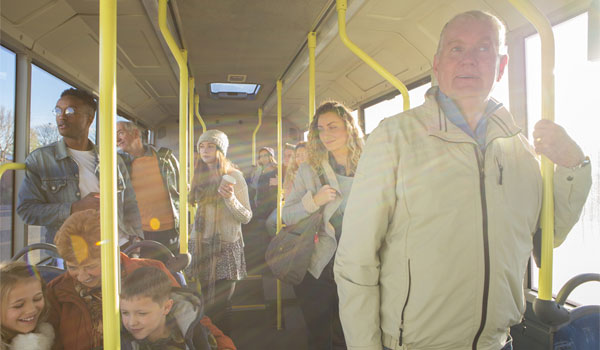 Ein Senior hält sich in einem vollen Bus an einer Stange fest.