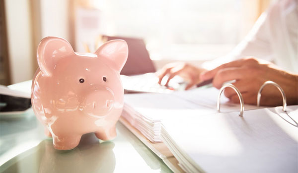 Sparschwein steht auf dem Schreibtisch, während ein pflegender Angehöriger seine Steuererklärung macht.