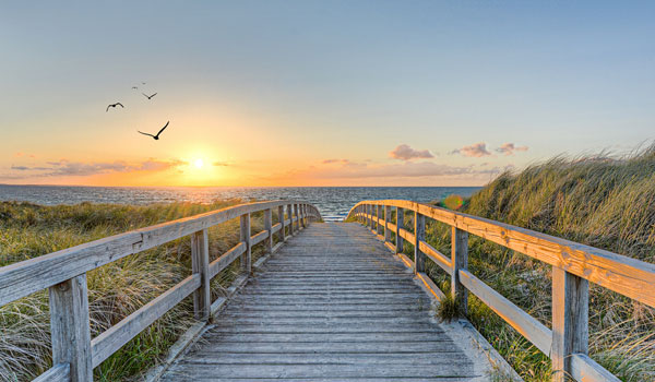 Hölzerner Steg von den Dünen zum Meer bei Sonnenuntergang.