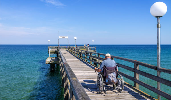 Ein Rollstuhlfahrer fährt an einem Steg am Meer entlang.