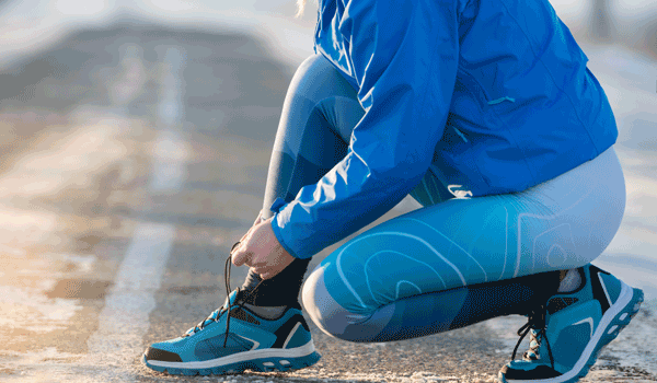 Eine Frau kniet auf dem Boden und schnürt sich die Sportschuhe zu.