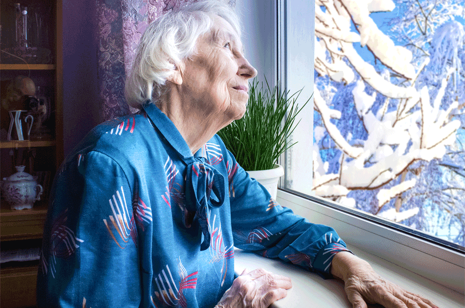 Eine ältere Dame schaut aus dem Fenster in den Schnee.