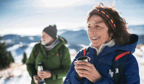 Eine Frau und ein Mann machen eine Pause bei ihrer Winterwanderung und trinken einen warmen Tee aus der Thermoskanne.