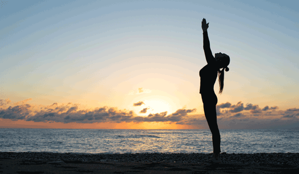 Ein Frau macht den Yoga Sonnenbruß am Meer.