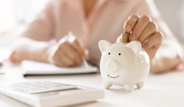 Eine Frau schmeißt eine Münze in ein Sparschwein.