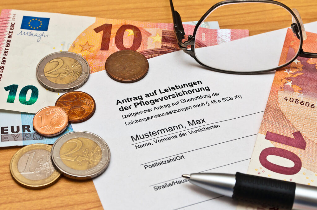 Ein Antrag auf Pflegegrad 1. Darüber liegen Euroscheine und Münzen.