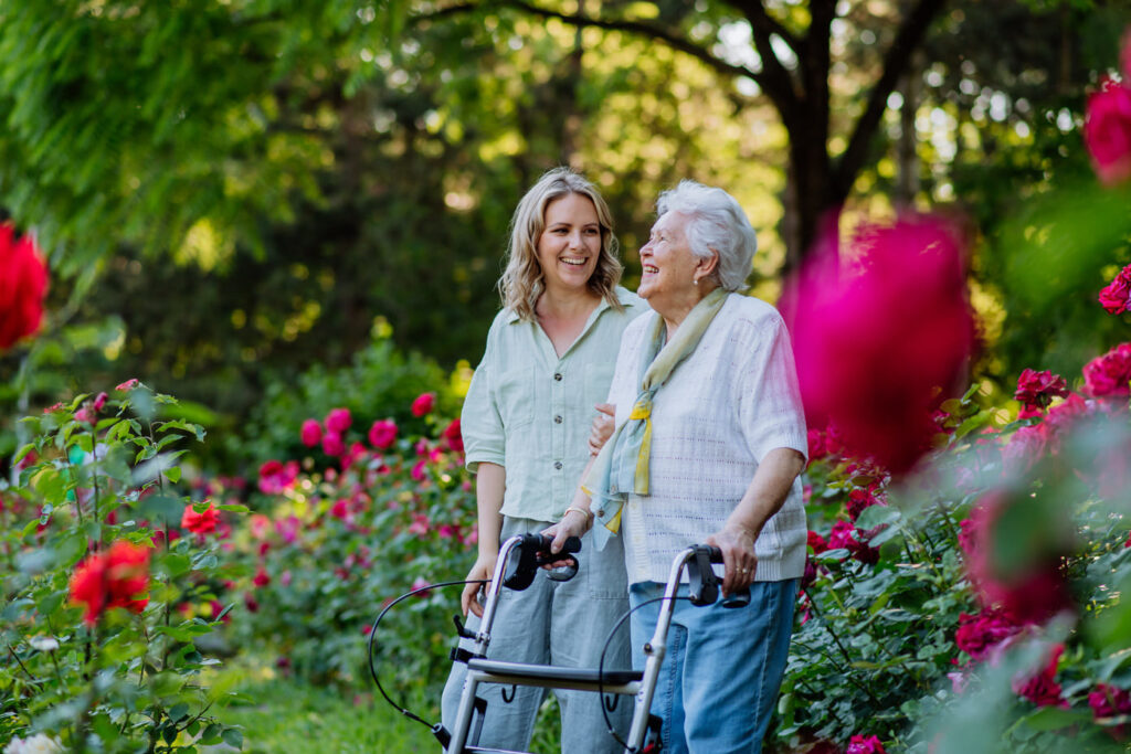 Eine ältere Frau mit einem Rollator geht mit einer Freundin im Garten spazieren