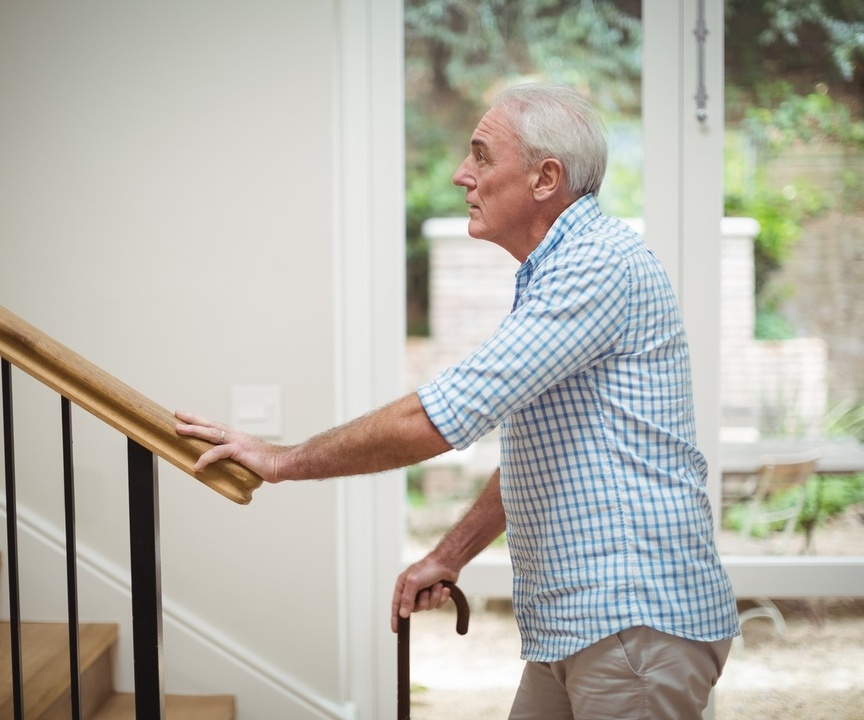 Ein Senior hat Knieschmerzen beim Treppensteigen und hält sich deswegen sein Knie.