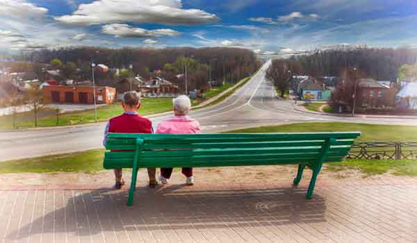 Ein Seniorenpaar auf einer Parkbank blickt auf ein Demenzdorf.