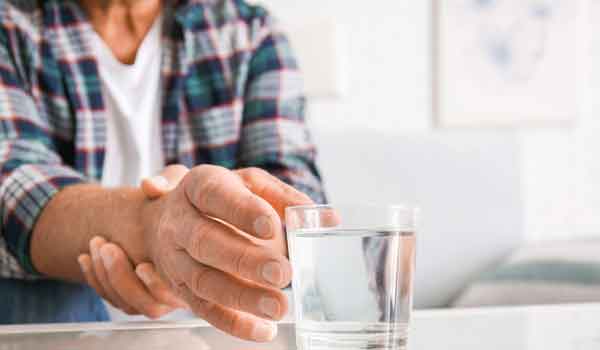 Ein Senior, welcher an Parkinson erkrankt ist, greift nach einem Wasserglas und hält dabei seinen Greifarm fest.