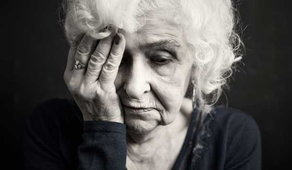 Eine depressive Seniorin hält sich den Kopf.