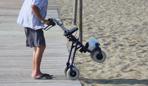 Ein Senior mit Rollator möchte vom Holzweg zum Strand zu gelangen.