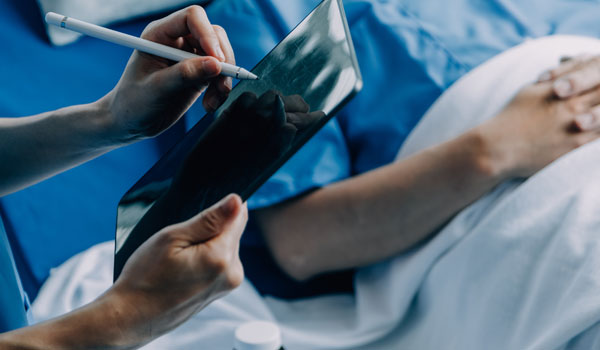 Ein Ärztin mit Tablett macht an einem Krankenbett eine Diagnose.